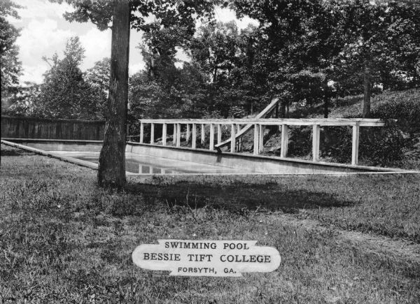 An outdoor swimming pool at Bessie Tift College stands among trees at the bottom of a hill. Bessie Tift College opened in 1907. Caption reads: "Swimming Pool, Bessie Tift College, Forsyth, GA."