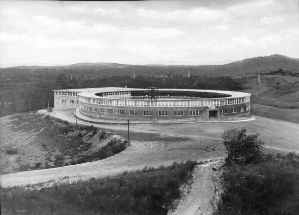 Elevated view of the exterior of Liberty Heights Swimming Pool, a circular structure standing on a hilltop. Stairs lead to a door labeled, "Exit," where a sign reads, "Entrance at Other End of Building, Don't Enter Here." The pool was built in 1919.