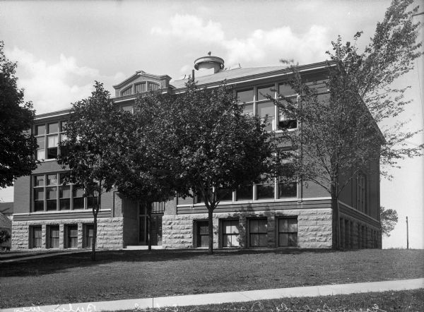 Exterior view of Green Lake County Training School, built in 1912. Trees stand before the entrance of the school, and a sidewalk passes through the front lawn.
