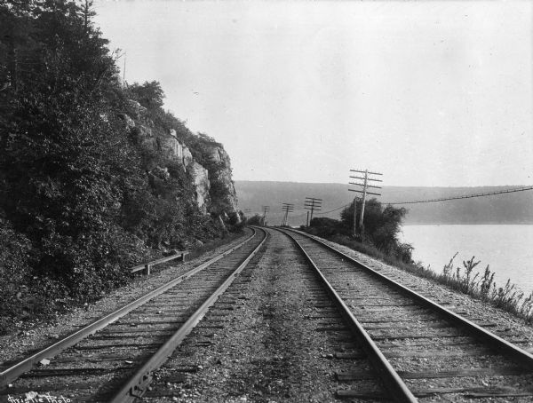 View of Chicago, Northwestern Railroad set of two railroad tracks at Devil's Lake, chartered in 1859. To the right, power lines run the length of the Devil's Lake shoreline.