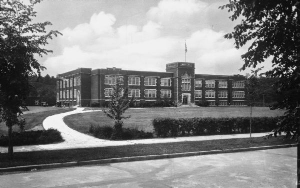 View from street toward a path that leads to the main and side entrances of the Eau Claire State Normal School. Automobiles are parked on the left side. The State Normal School was established in 1916.