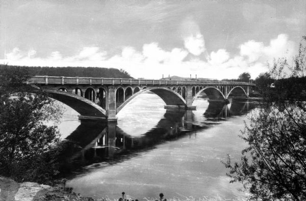View from shoreline toward the Water Street Bridge, connecting Summit Avenue to Water Street. The structure of the bridge is made up of small and large arches. The bridge suffered two collapses, one in 1884 and another in 1945.