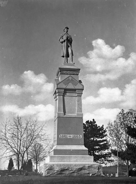 View of the Soldier's Monument, erected in 1898 at Evergreen Cemetery, sponsored by the Grand Army of the Republic. The monument, featuring a soldier and two United States flags, memorializes the soldiers of the Civil War. Headstones are behind the monument.