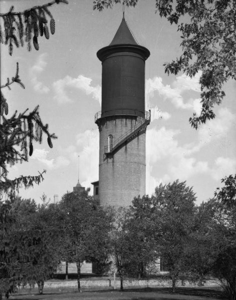 View of a water tower built in 1901. Trees surround the structure and other buildings are in the background.