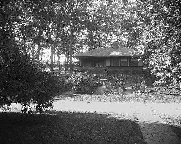 View of Dering's Resort, located in a wooded area. In the foreground is a road, and on the other side is a resort cabin with a small garden and bird bath.