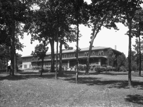 Exterior of Sherwood Forest Hotel, opened around 1873 by John C. Sherwood. The view includes trees in the foreground, and plants surround the two-story hotel.