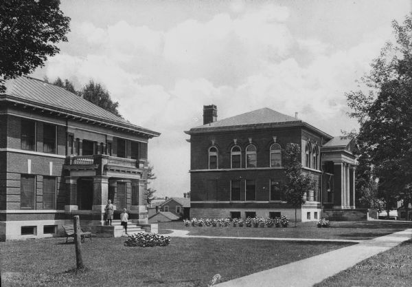 View of the Green Lake County Courthouse and Jail. Two children stand on the steps of the jail, built in 1869. The courthouse, built in 1863, is on the right.