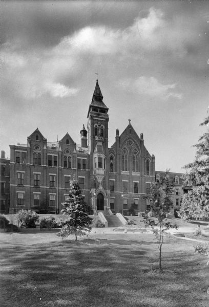 Exterior of the chapel at Saint Clara Academy, built in 1852. Founded by Father Samuel Mazzuchelli, the academy's chapel features elaborate stained glass windows and stairs leading to a main entrance. A tower topped by a cross stands at the middle of the building.