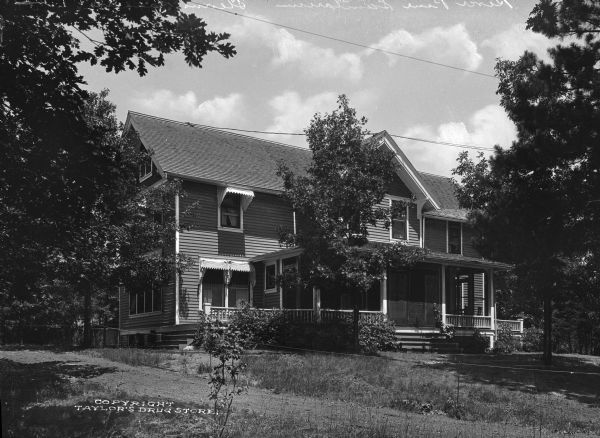 Exterior of River Pine Sanitarium, which opened in 1906. A dirt driveway leads past the sanitarium building which features a porch with outdoor furniture.