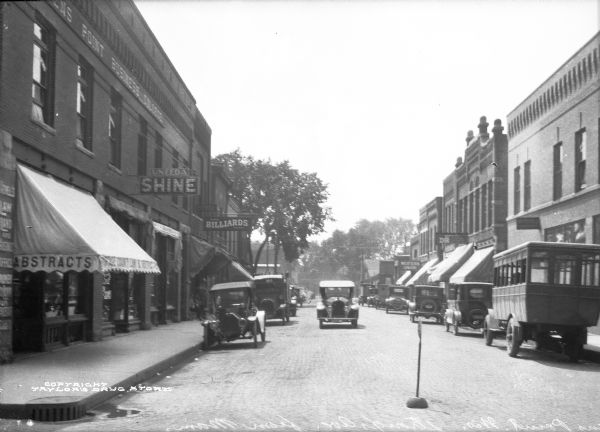 View down Strong's Avenue, taken from Main Street. An automobile drives past other parked cars and storefronts.