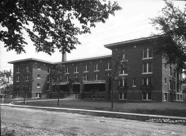 Exterior view of Nelson Hall, a girls' dormitory built in 1915 for the State Normal School system. A path leads to the brick building's main entrance and porch.