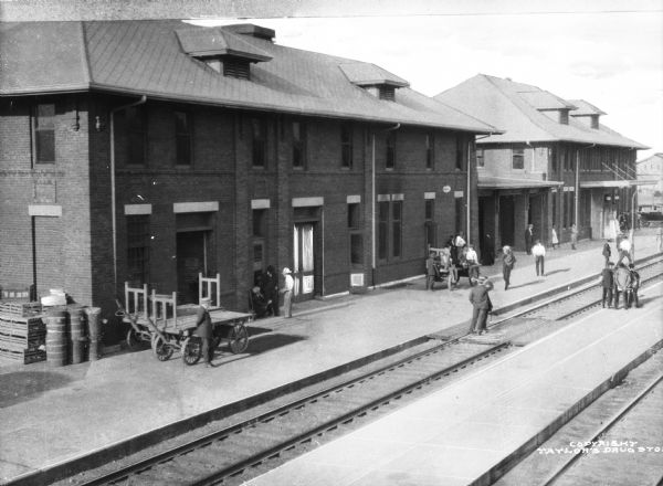 Elevated view of the depot at the Southside Railroad Complex, which began operation in 1871. Adults and children stand near the railroad tracks outside of the depot.