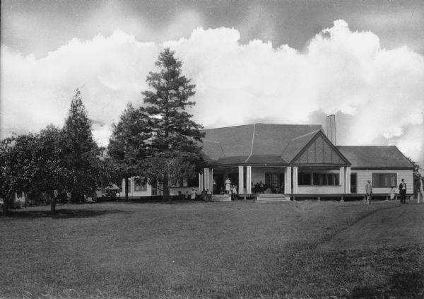 Exterior of the Door County Country Club, opened in 1921. Men and women gather on the building's porch and on the lawn.