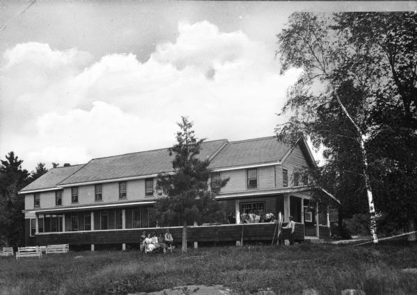 Exterior of Bay Shore Inn, which opened in 1922. Men and women gather on the porch and on the lawn in front of the building.