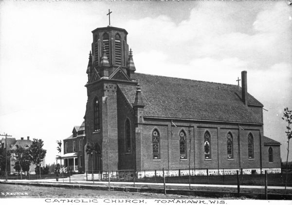 Exterior of the Saint Mary's Catholic Church. The view from across the street features the church building's stained glass windows and belfry. Caption reads: "Catholic Church, Tomahawk, Wis."