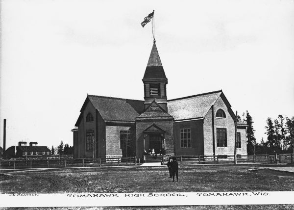 Exterior of Tomahawk High School, a brick building featuring four wings and a main entrance. Adults and children stand on the school's porch and lawn. Caption reads: "Tomahawk High School, Tomahawk, Wis."