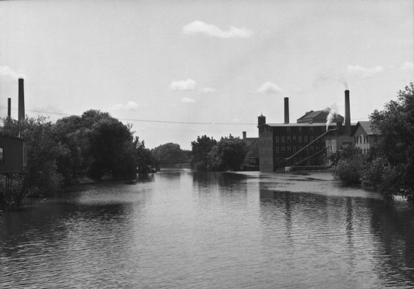 View of Rock River from the Main Street Bridge. On the right industrial buildings are along the shoreline, and a bridge is in the distance.