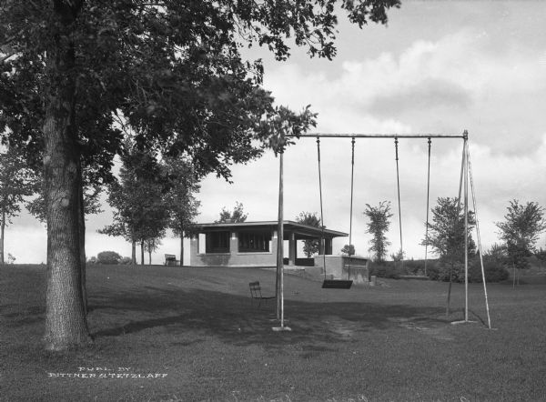 View of Riverview Park. The view features a shelter, benches, and a swing set among trees.