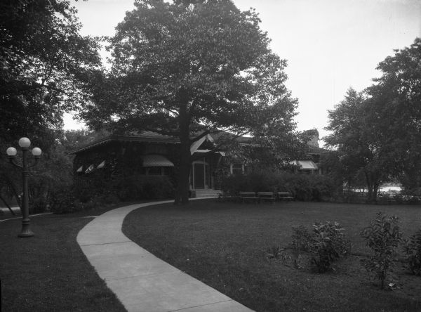 View of a park featuring a residential-type shelter. Lampposts and benches stand on the lawn.