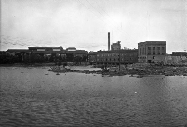 View across water toward the Consolidated Paper Company Offices and Mills, which formed in 1894. The buildings are on the bank of the Wisconsin River.