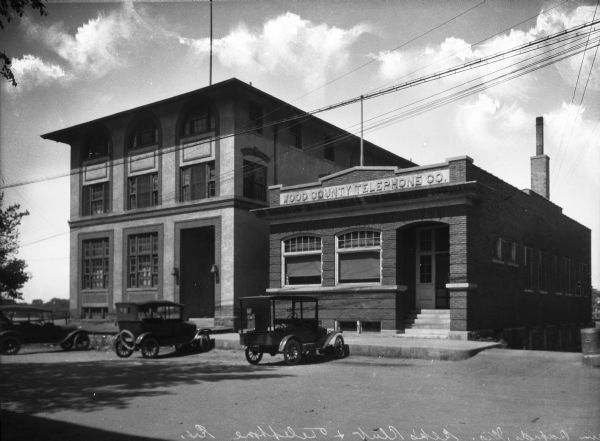 Exterior of the Elks Club and the Wood County Telephone Company. Automobiles are parked in front of the two buildings.