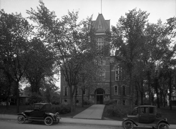 Front view of the Wood County Courthouse, built in 1866 by Lyman Howe and John Rablin. The brick building features an arched entrance, and automobiles are parked outside. The courthouse burned in 1885.