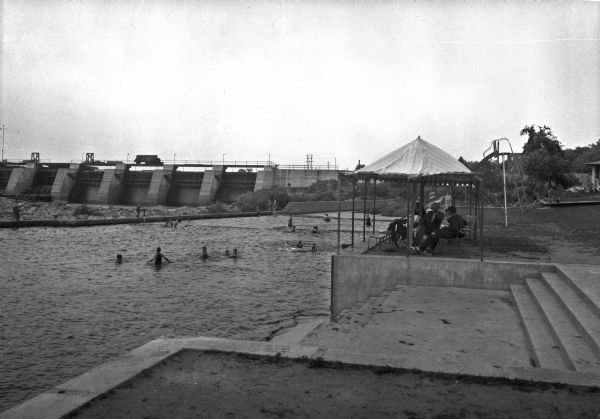 Adults sit beneath a tent alongside a swimming pool overlooking Stora Enso Dam. The dam was built by the Consolidated Water Power Company in 1903.