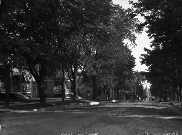 View down Capron Street, a dirt road in a residential area. There is a clocktower on a building in the distance.