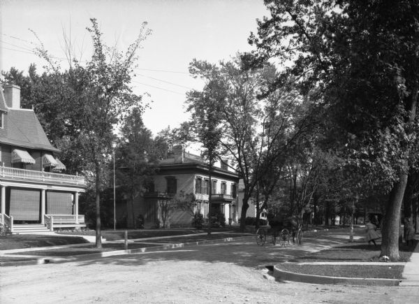 View down North Washington Street, a residential area. Two girls are running on the terrace toward a man sitting in a horse-drawn carriage.