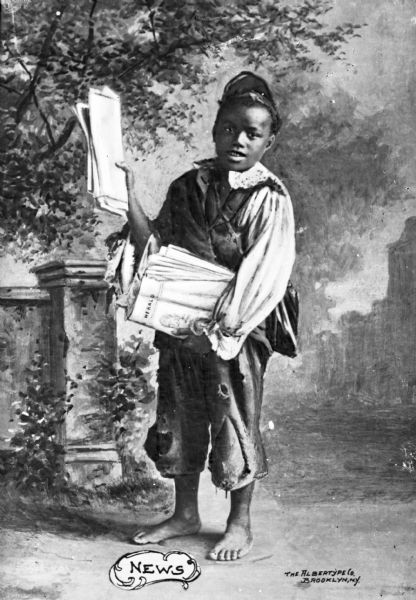 Studio portrait of an African American boy dressed in the costume of a stereotypical newsboy. The child holds up a newspaper in one hand and holding a stack of newspapers under the other arm while standing in front of a painted background.