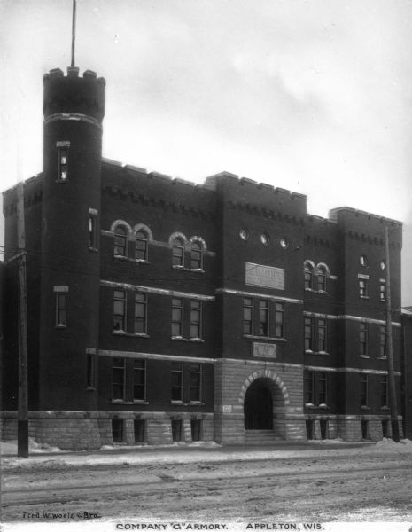 Exterior view from across street of the armory featuring a turret on the left of a main arched entrance. Caption reads: "Company "G" Armory, Appleton, Wis."