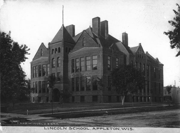 Exterior view from across street of Lincoln School, which opened in 1898.  A wide lawn leads to the building's arched entrance and central pavilion. Caption reads: "Lincoln School, Appleton, Wis."