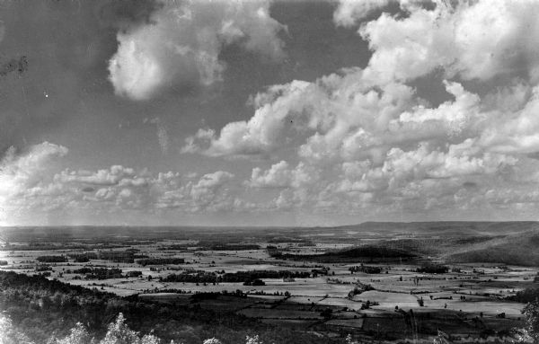 Elevated view of farmland with cumulus clouds overhead.