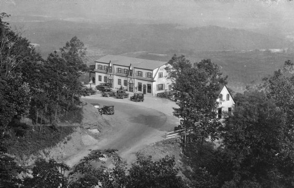 Elevated view of the Blue Ridge Terrace, a large hotel on a mountain overlooking the valley. Cars are parked near the road, and three men are gathered on the porch to the left.