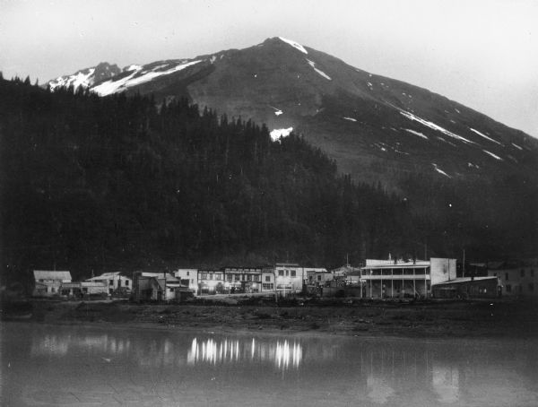 View across water towards the 4,462-foot Marathon Mountain at midnight. Houses and establishments are along the shoreline. A bar is labeled, "The Commerce," and "Olympia Beer."