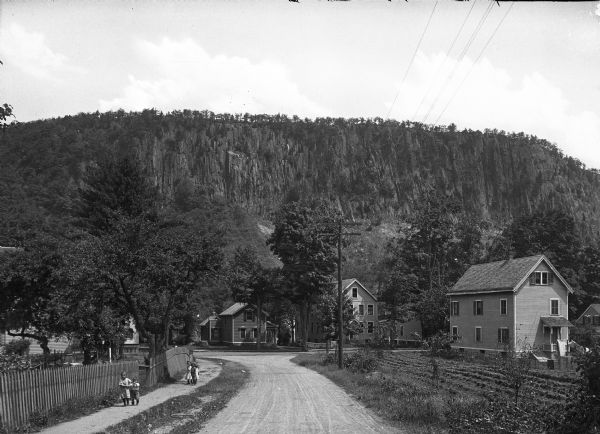 View down road towards houses with a rock formation in the distance. Children are walking on the sidewalk on the left.