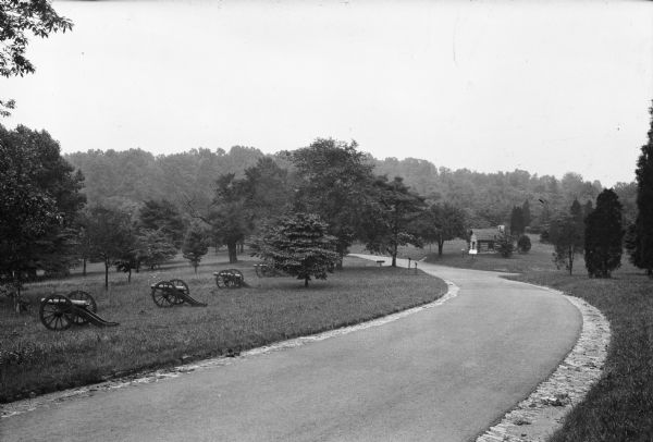 View of Inner Line Drive at Gulph Road.  Canons line the left side of the road and a reconstructed cabin stands on the right.