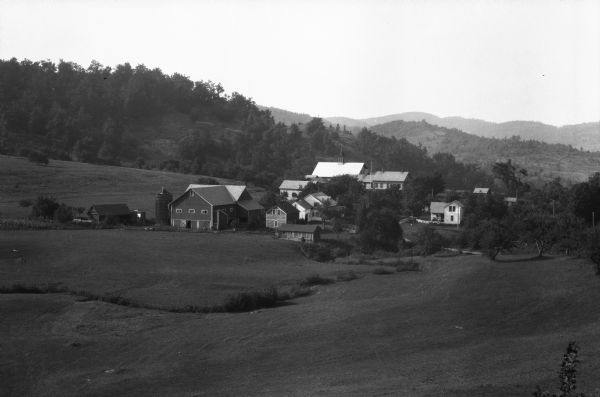 View of a farm estate and barn. Fields and hills surround the buildings.