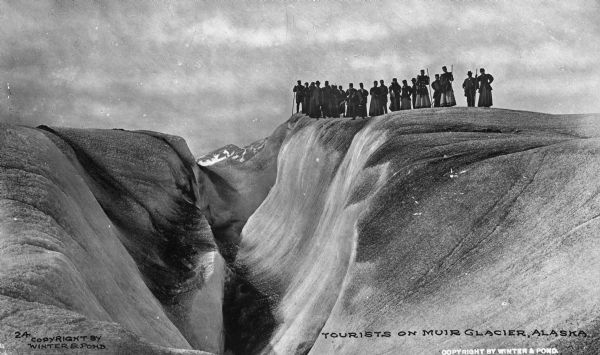 View of a tourist group on Muir Glacier near a ravine. Caption reads: "Tourists on Muir Glacier, Alaska."
