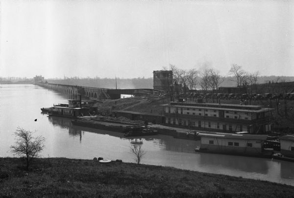 View down hill of Wilson Dam, which opened in 1924. Located on the Tennessee River, boats and buildings are near the dam on the opposite shoreline.