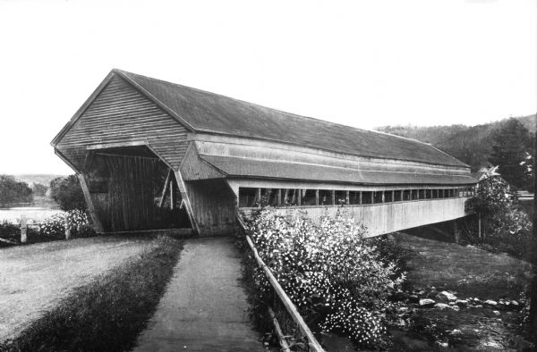 View along sidewalk and road toward a wooden covered bridge.