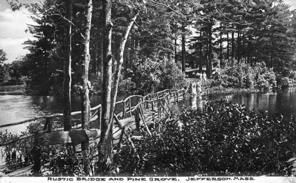 View of a rustic bridge crossing a river surrounded by foliage and a pine grove. Women and children stand on the bridge and along the opposite bank. Caption reads: "Rustic Bridge and Pine Grove, Jefferson, Mass."