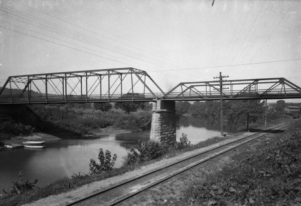View across railroad tracks toward a railroad bridge spanning Hocking River. Boats are moored along the left bank.