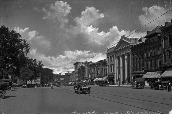 Storefronts line either side of Main Street near the Northampton National Bank, a neoclassical building. Trolleys, automobiles, and people crowd the street and sidewalks.