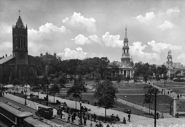 Elevated view of a city, featuring the Trinity (1813-1814), United (1812-1815), and Center Churches (1812-1814) and the Phelps Gateway.  People gather on the sidewalk near automobiles and trolley cars.