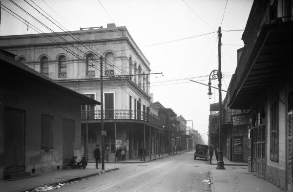 View down Nicholas and Royal Streets. Men stand on the sidewalk near a cafe and lunch room.
