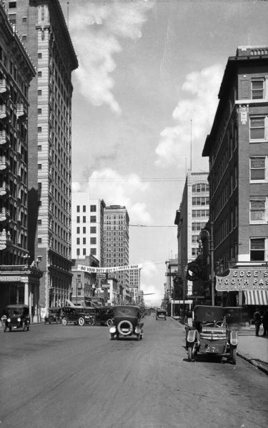 View down Main Street featuring tall buildings, automobiles, and a banner reading, "Do Your Duty - Buy a Liberty Bond."
