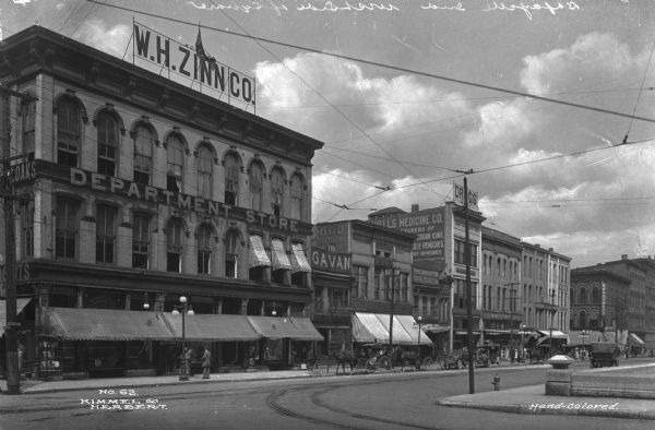 View of the business district looking toward North Third Street. W.H. Zinn Co. Department Store, an Italianate building constructed in 1837, stands on the corner of North Third Street and Columbia Street. Horse-drawn carriages and automobiles are parked along the street in front of storefronts.