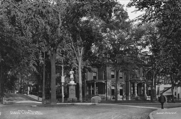 View of North Adams Public Library from a street intersection. The building was designed in the Victorian style and renovated for library use in 1897 by architect Edwin T. Barlow. The view features the Civil War Soldiers' Monument, dedicated on July 4, 1878.