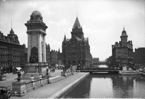 View of Masonic Park featuring the Erie Canal and the Soldiers and Sailors Monument, dedicated in 1909. The Empire House can be seen at left, constructed in 1845 by John L. Tomlinson. On the right bank of the canal stands the Gridley Building, designed in 1867 in the Second Empire style by architect Horatio Nelson White.